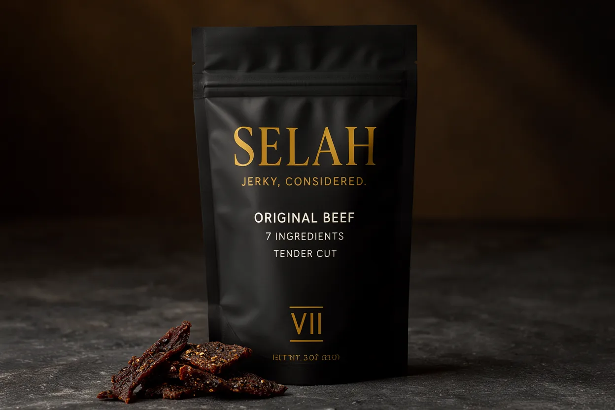 A single matte black Selah Jerky Original Beef pouch standing on a dark stone surface, with a small pile of jerky pieces at its base